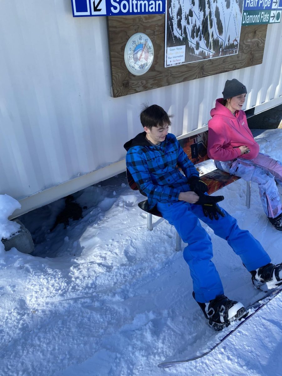 Brody Lynch and Ava Fairley strap up boots at the top of Snowhaven on a bench.