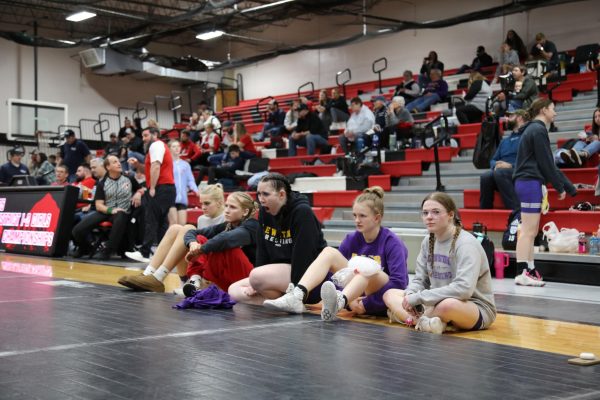 Members of the girls wrestling team watch their teammate from the edge of the mat