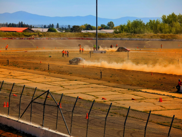 2 competing cars kicking up dust trails on the track.